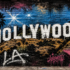 Graffiti-style illustration of the Hollywood Sign painted on a brick wall with palm trees, stars and vintage movie imagery.