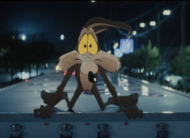 Wile E. Coyote sits at a courtroom table beside live-action actors in a scene from Coyote vs. Acme