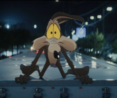 Wile E. Coyote sits at a courtroom table beside live-action actors in a scene from Coyote vs. Acme