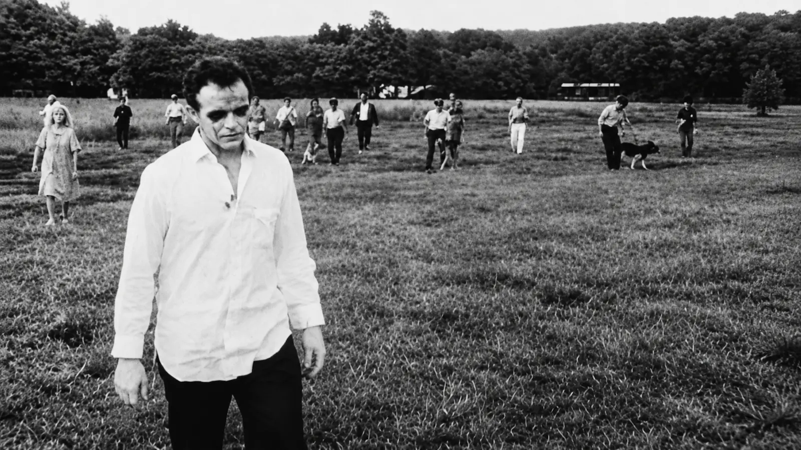 A ghoul in a white shirt stands in a field as the armed posse and their dogs close in behind him in Night of the Living Dead (1968), one of the most influential low-budget horror films.